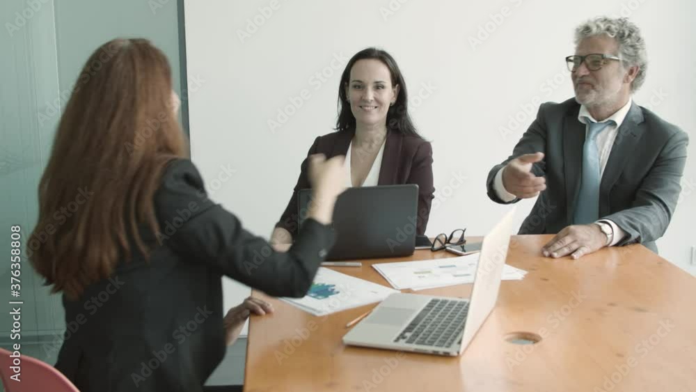 Young female manager shaking hands with partners over meeting table with paper charts and laptops. Slow motion, rear view. Handshake concept Young female manager shaking hands with partners over meeting table with paper charts and laptops. Slow motion, rear view. Handshake concept