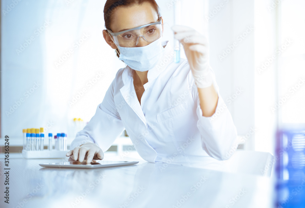 Female laboratory assistant analyzing test tube with blue liquid. Medicine, health care and researching concept Female laboratory assistant analyzing test tube with blue liquid. Medicine, health care and researching concept