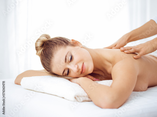 Young and blonde woman enjoying massage of back in spa salon. Beauty concept