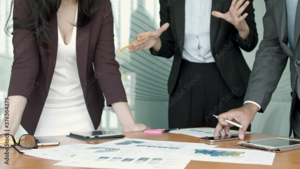 Business group analyzing paper reports, standing at table with documents with graphs, pointing at charts, discussing diagrams. Dolly, cropped shot. Teamwork and analysis concept Business group analyzing paper reports, standing at table with documents with graphs, pointing at charts, discussing diagrams. Dolly, cropped shot. Teamwork and analysis concept