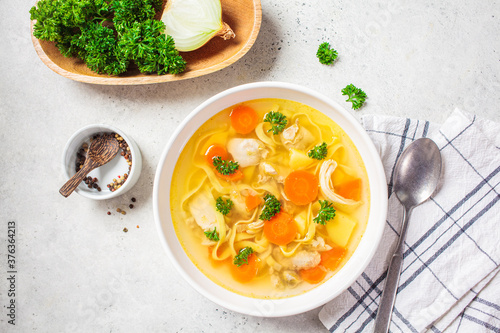 Homemade chicken soup with noodles and vegetables in white bowl, white background, top view. photo