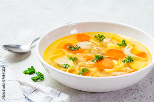 Homemade chicken soup with noodles and vegetables in white bowl, white background. Healthy warm comfortable food.