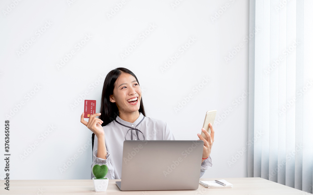 The Asian businesswoman's hand is holding a credit card and using a smartphone and laptop for online shopping internet payment in the office The Asian businesswoman's hand is holding a credit card and using a smartphone and laptop for online shopping internet payment in the office