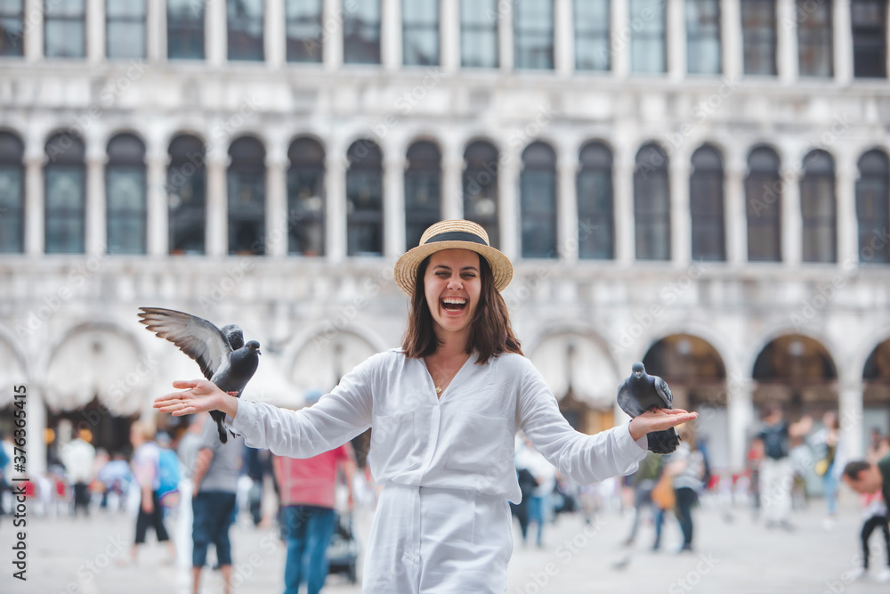 woman in white clothes with straw hat having fun with pigeons at venice city square