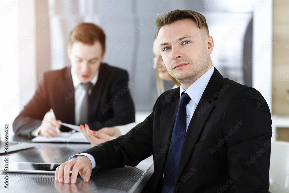 Businessman headshot at meeting in sunny office. Unknown entrepreneur sitting with colleagues at the background Businessman headshot at meeting in sunny office. Unknown entrepreneur sitting with colleagues at the background
