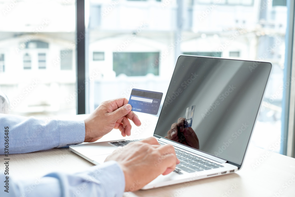 The businessman's hand is holding a credit card and using a laptop for online shopping and internet payment in the office The businessman's hand is holding a credit card and using a laptop for online shopping and internet payment in the office