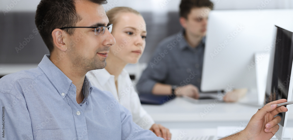 Business people working together in modern office. Happy smiling adult businessman using pc computer with colleagues. Teamwork and partnership concept Business people working together in modern office. Happy smiling adult businessman using pc computer with colleagues. Teamwork and partnership concept