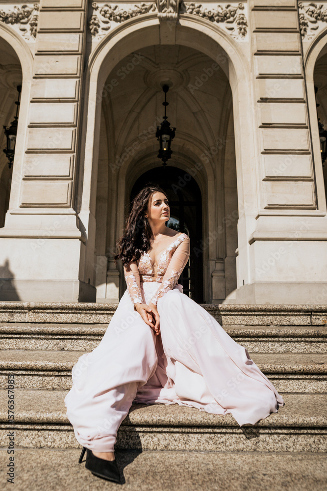 Naklejka premium Beautiful attractive woman stand on stairs in pink dress and look away