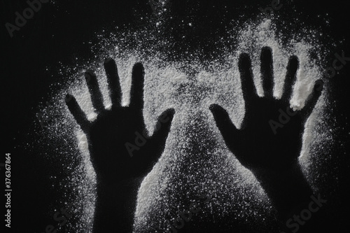 Plain flour in a shape of human hands on black wooden table