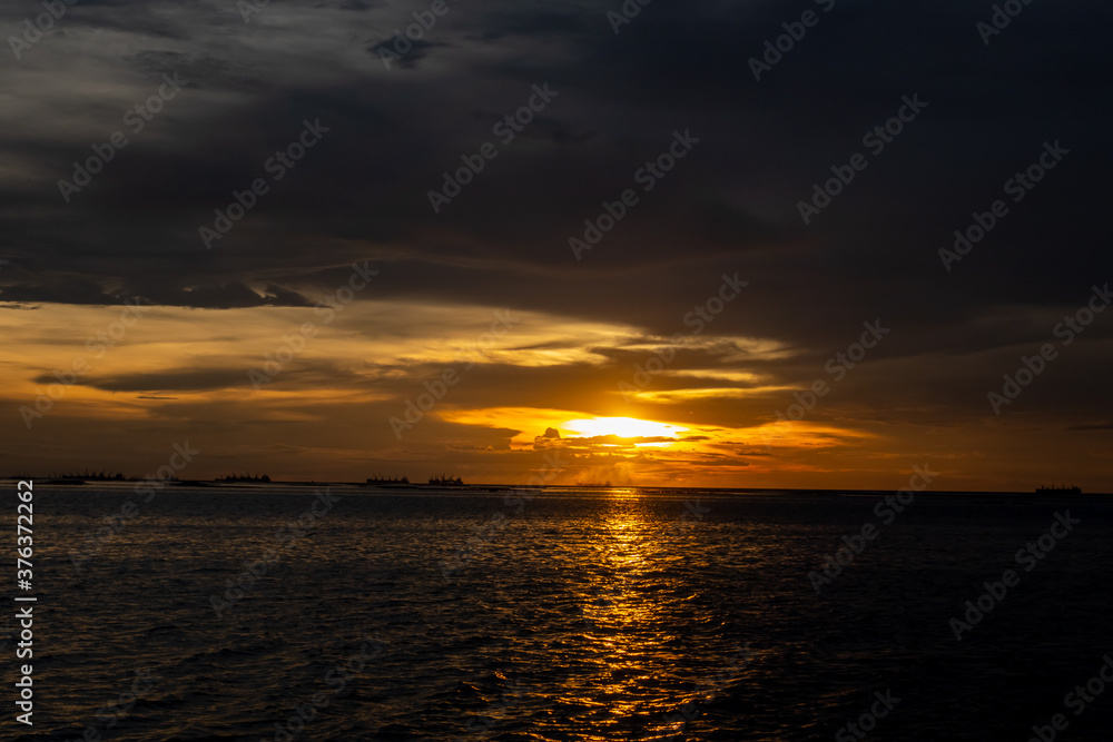Evening sunset over the sea during the tropical monsoon rain season with distant cargo ships waiting to enter the dockyard