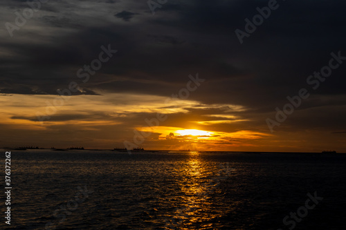 Evening sunset over the sea during the tropical monsoon rain season with distant cargo ships waiting to enter the dockyard