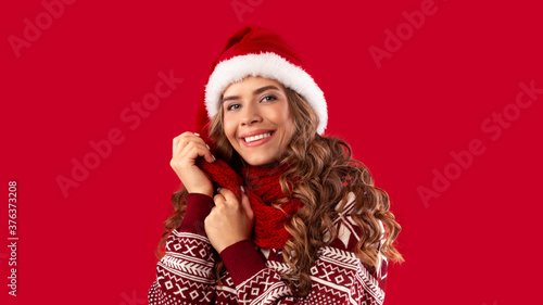 Portrait of sweet young lady wearing woolen sweater  Santa hat and scarf on red background