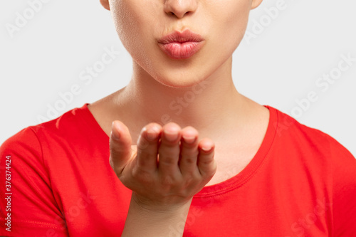 Blowing kiss. Feeling love. Close up woman in red t-shirt pouting lips and opened hand. Isolated on neutral. Affection and desire. Romantic emotion