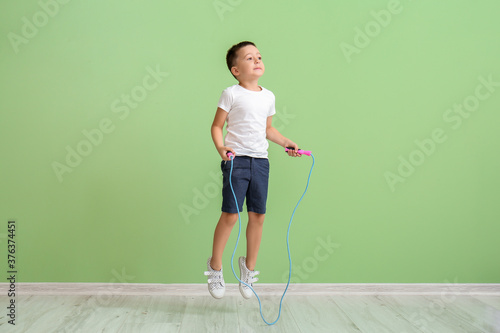 Cute little boy jumping rope near color wall photo