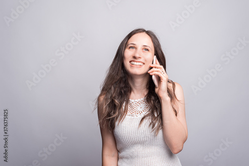 Photo of cute young woman talking on smartphone with someone over white wall © Vulp