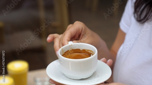 Close up of young woman holding a cup of an espresso in coffee place. Coffee culture