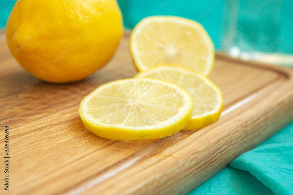 Lemon and slices of yellow lemon lie on a wooden cutting board on a background of turquoise fabric. Tropical fruits. Fresh citrus. Free space for text. Top view Lemon and slices of yellow lemon lie on a wooden cutting board on a background of turquoise fabric. Tropical fruits. Fresh citrus. Free space for text. Top view