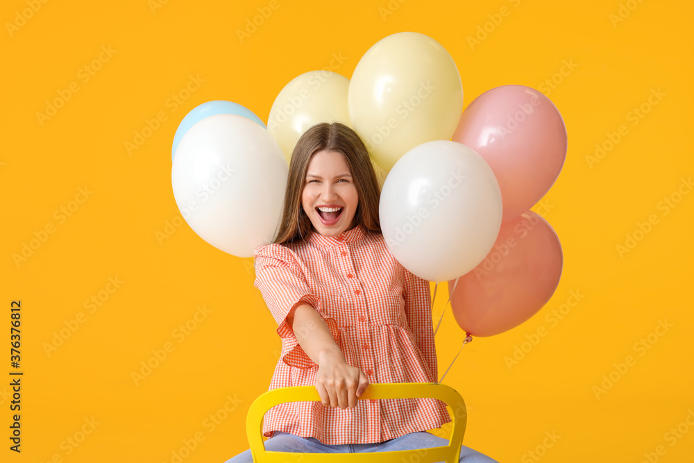 Young woman with balloons sitting on chair against color background Young woman with balloons sitting on chair against color background