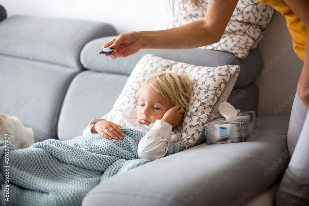 Sick child, toddler boy lying on the couch with his white puppy in living room with fever, resting Sick child, toddler boy lying on the couch with his white puppy in living room with fever, resting