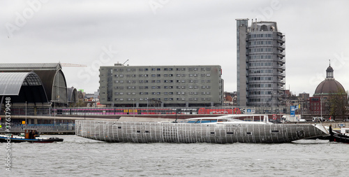 Aluminium hull. Transport of a super yacht hull on a pontoon with tugboats at the river. . Ship building industry. Super sailing yacht. Netherlands. Het IJ. Amsterdam. Central station.