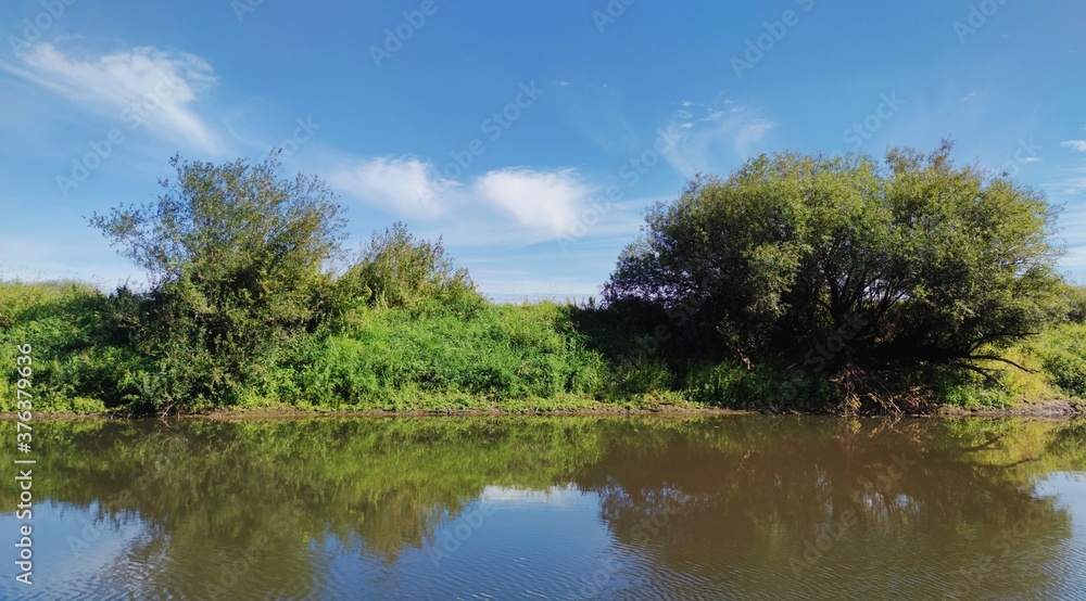 sunny panoramic landscape with green bank of a small river