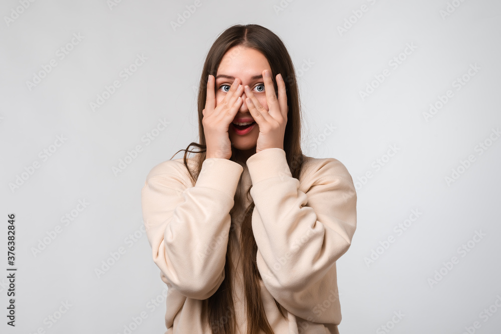 Young beautiful brunette woman covering face and eyes with hand, looking through fingers Young beautiful brunette woman covering face and eyes with hand, looking through fingers