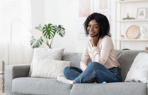 Shy Black Girl Sitting On Sofa At Home, Posing To Camera