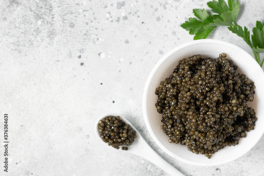 Black caviar. Black sturgeon caviar in a ceramic bowl and in a ceramic spoon on a light background. Useful delicacy. Top view with space for text Black caviar. Black sturgeon caviar in a ceramic bowl and in a ceramic spoon on a light background. Useful delicacy. Top view with space for text