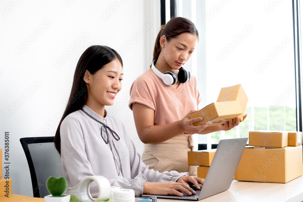 Asian woman business two people owner with many parcel boxes on the table happy online sales job, use your laptop, get an order from customers, take notes, and make arrangements for delivery by post Asian woman business two people owner with many parcel boxes on the table happy online sales job, use your laptop, get an order from customers, take notes, and make arrangements for delivery by post