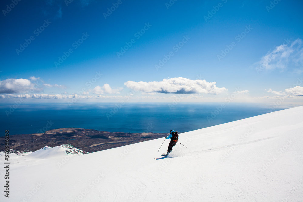 A female skier skiing down a volcano and the Atlantic ocean in the background, Iceland