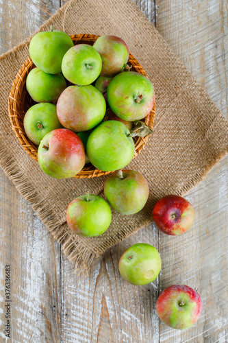 Apples in a wicker basket on wooden and piece of sack background. top view.