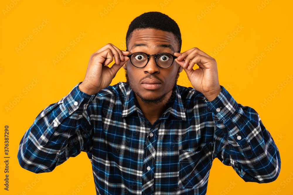 Amazed African American Looking At Camera Through Eyeglasses, Yellow Background Amazed African American Looking At Camera Through Eyeglasses, Yellow Background