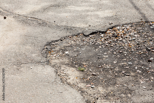 Damaged asphalt pavement road with potholes caused by freeze and thaw cycle during winter. © Elena