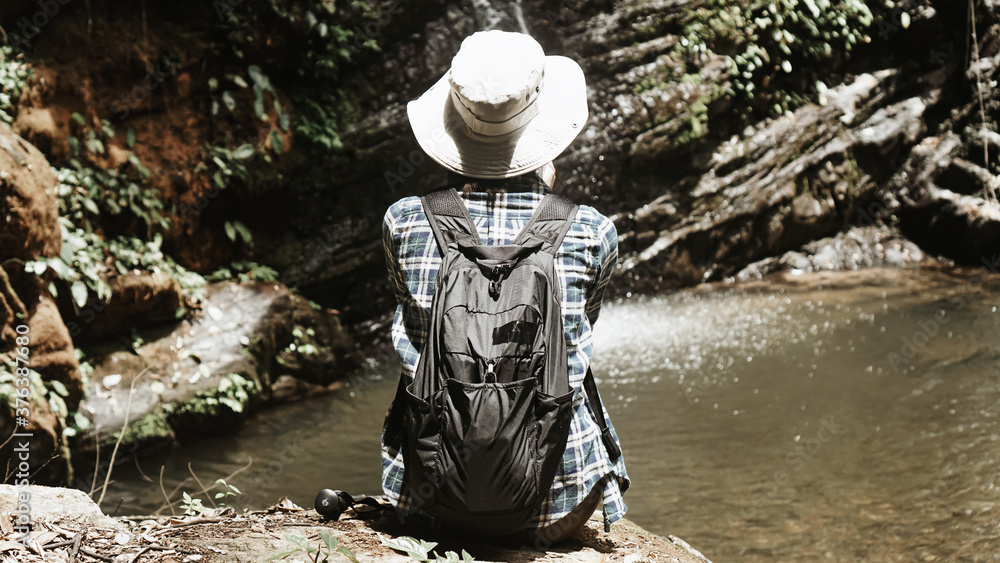 Young girl tourist traveling backpack enjoying adventure exploring nature jungle trail tracking into forest reaching waterfall, wearing travel gear hat and camera,lifestyle.selective focus.