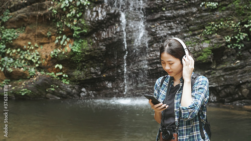 Young girl tourist traveling backpack enjoying adventure exploring nature jungle trail tracking into forest reaching using headphone listening to music, outdoor freedom lifestyle.selective focus.