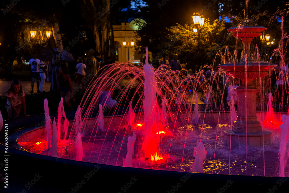 ODESSA, UKRAINE - August 4, 2018: tourists and guests of the city are resting in the city park near the musical colorful fountain in the evening. Light fountain show in a night park ODESSA, UKRAINE - August 4, 2018: tourists and guests of the city are resting in the city park near the musical colorful fountain in the evening. Light fountain show in a night park