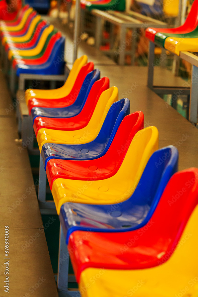 Multicolored Empty plastic chairs in the stands of the stadium. Many empty seats for spectators in the stands. Empty plastic chairs for football fans in the gym. Bright colorful seats for stadium fans