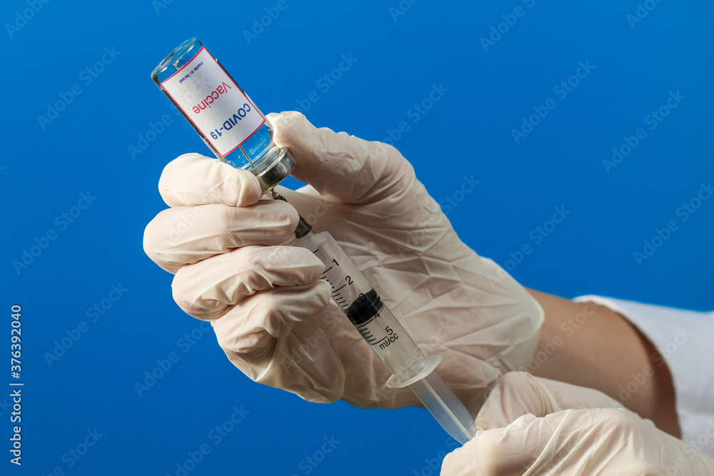 A doctor wearing medical gloves draws a medicine from a test tube with a COVID-19 vaccine and the inscription A doctor wearing medical gloves draws a medicine from a test tube with a COVID-19 vaccine and the inscription