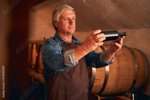 Good-looking man in apron holding bottle of wine photo