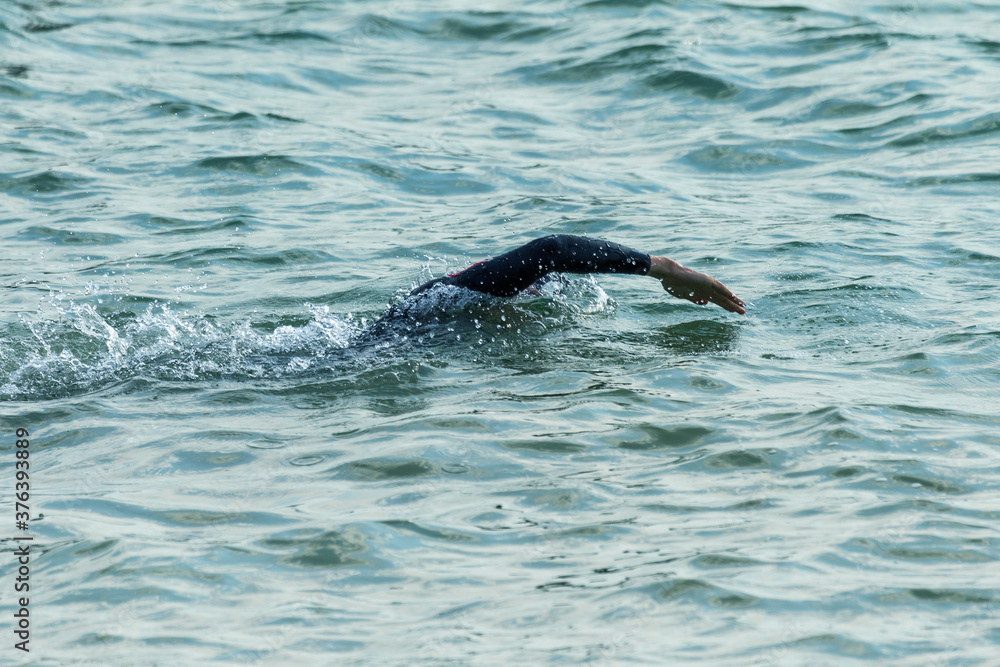 Obraz premium Swimmer swims in sea. Athlete triathlete swimmer drains from water. A professional athlete in triathletes trains for an ironman. The sportsman beautifully floats in blue sea water at competitions