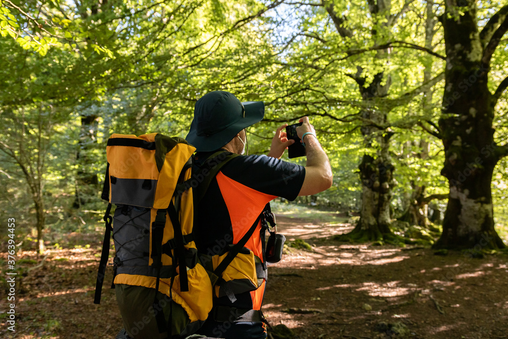 Naklejka premium Hombre con mascarilla haciendo una foto en el bosque con su teléfono móvil