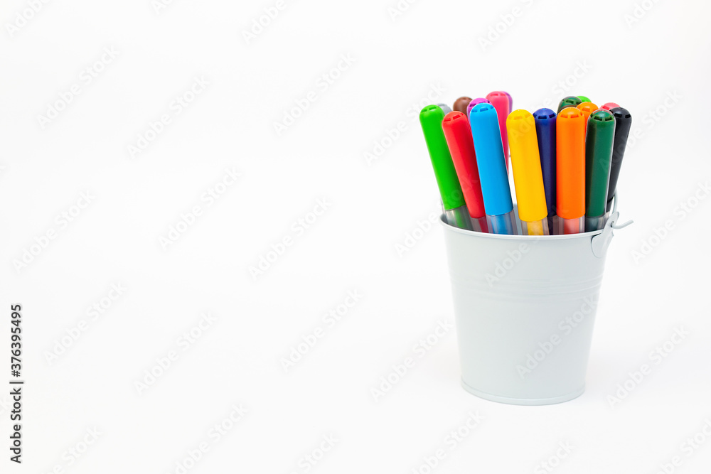Fototapeta premium Set multicolored pointed markers in a white metal bucket on light background, copy space. Drawing felt-tip pens, pencils, artists tools, creativity, leisure, hobby. Colorful school supplies.