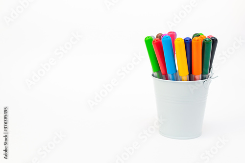 Set multicolored pointed markers in a white metal bucket on light background, copy space. Drawing felt-tip pens, pencils, artists tools, creativity, leisure, hobby. Colorful school supplies.