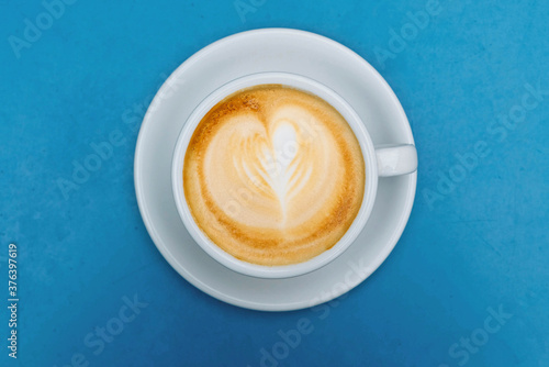 Cappuccino coffee in white cup with latte art on blue background.