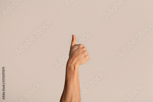 Cropped view of young guy showing thumb up gesture, expressing approval on light background