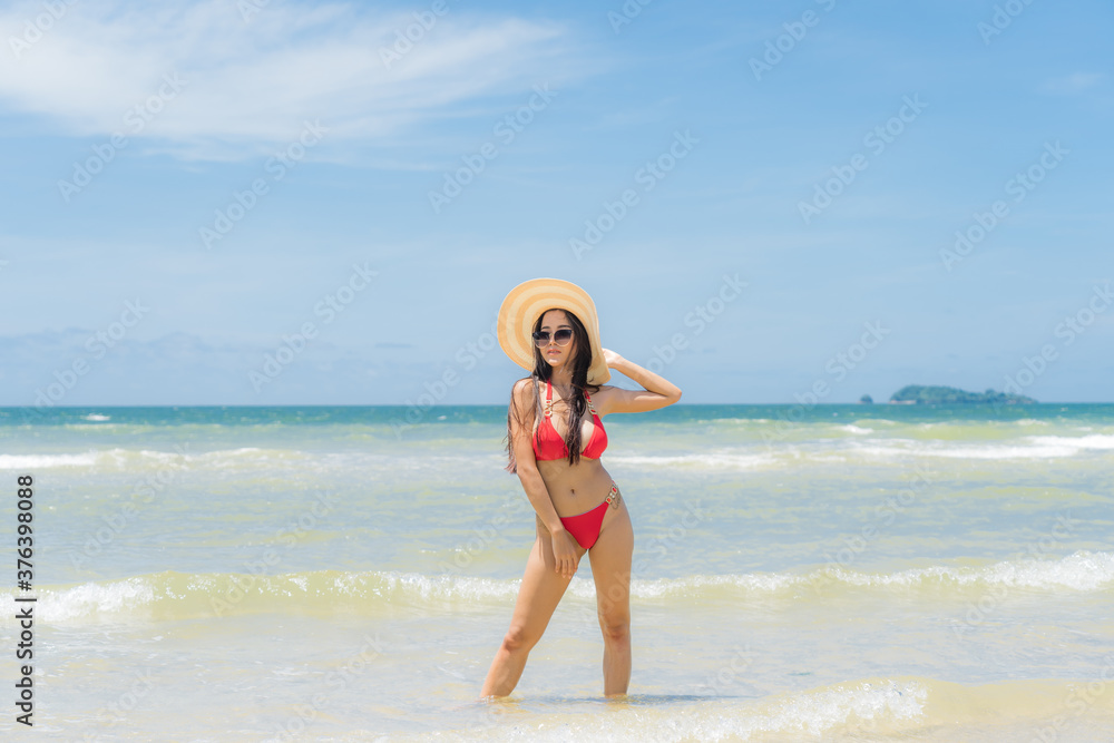 Asian woman wear a colourful bikini stand sunbathing on the sandy beach in a bright day and happy holidays with blue sky Asian woman wear a colourful bikini stand sunbathing on the sandy beach in a bright day and happy holidays with blue sky