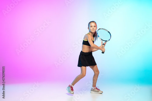 Running high. Little tennis girl in black sportwear isolated on gradient background in neon light. Little caucasian model, sport kid training in motion and action. Sport, movement, childhood concept. © master1305