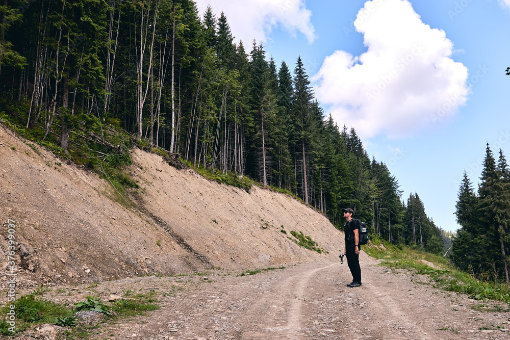 Man climbs uphill mountain. Sporty clothes and backpack Hiking through forest in summer. A path between fir and pine-tree during a sunny day. Dark autumn forest. Hiking in wild mountain. 