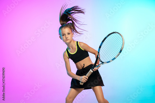 Winner. Little tennis girl in black sportwear isolated on gradient background in neon light. Little caucasian model, sport kid training in motion and action. Sport, movement, childhood concept. © master1305