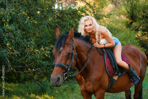 The girl sits on a horse and poses against the background of the forest.